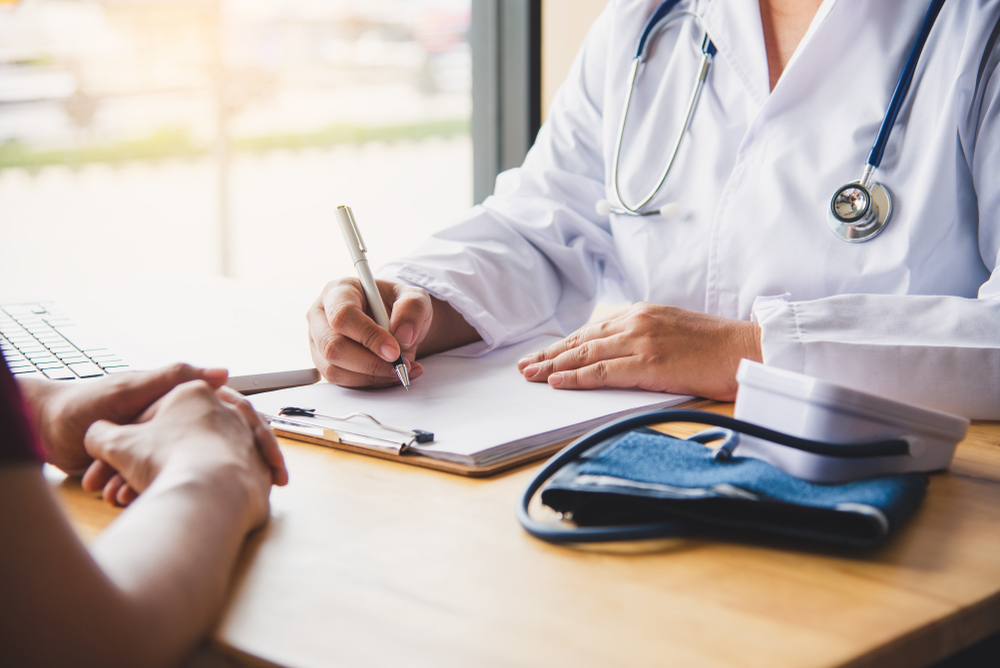 Doctor speaks with patient across desk, filling out paperwork