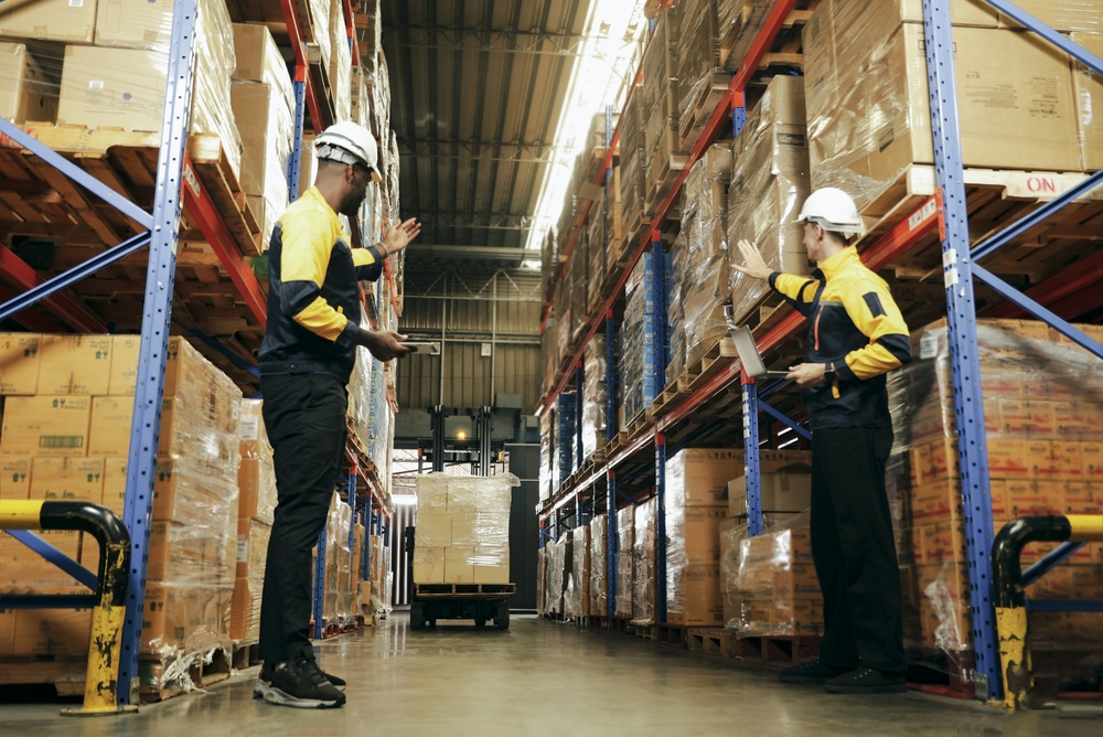 Warehouse workers in safety gear guiding a forklift through an aisle